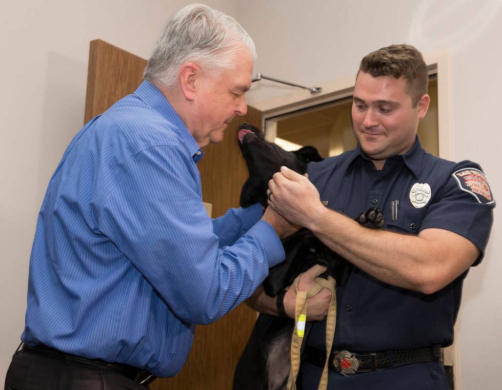 Gov. Steve Sisolak, left, pets a black lab puppy named Blaze, held by Las Vegas Fire and Rescue ...