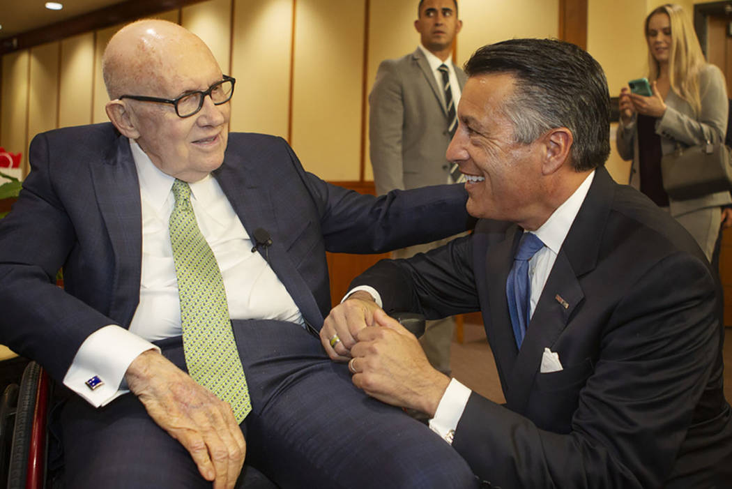 Former U.S. Sen. Harry Reid, left, pats the back of former Nevada Gov. Brian Sandoval, right, b ...