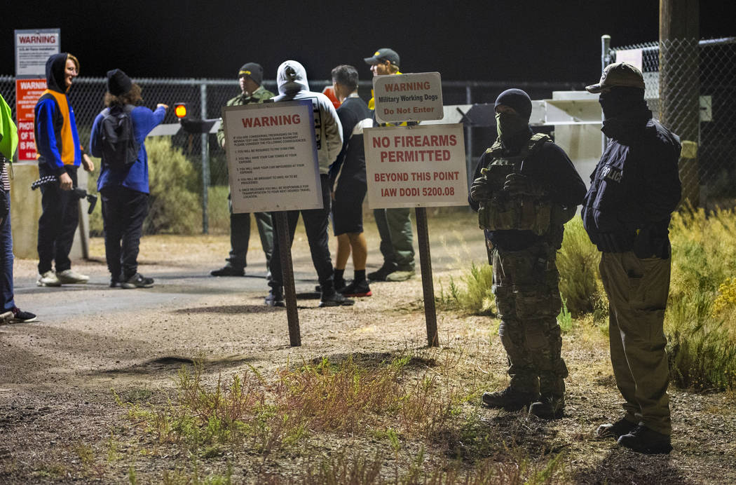 Security personnel and attendees stand along the fence line near the back gate of Area 51 in ho ...