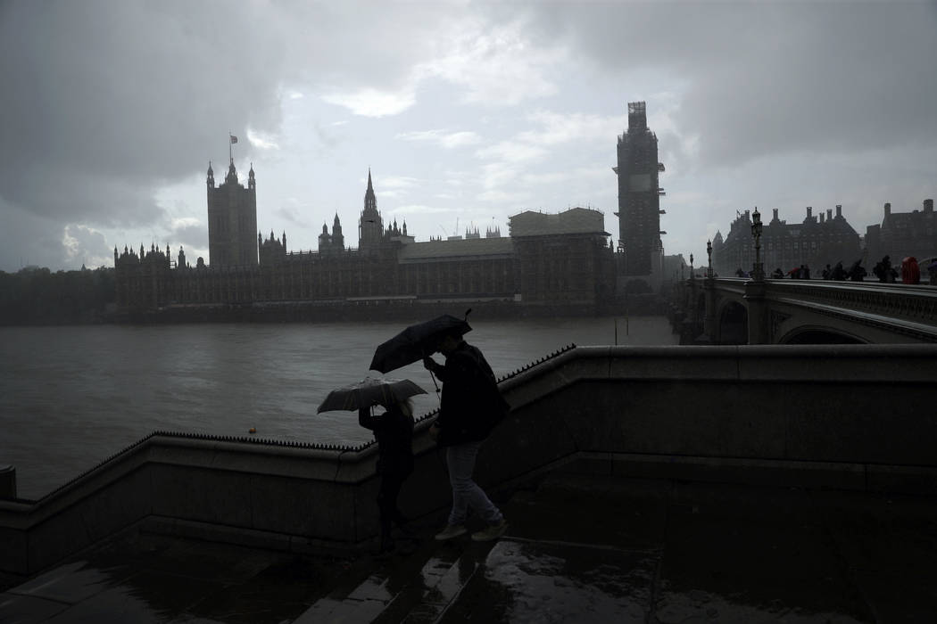 People are silhouetted with umbrellas in the rain backdropped by the Houses of Parliament in Lo ...