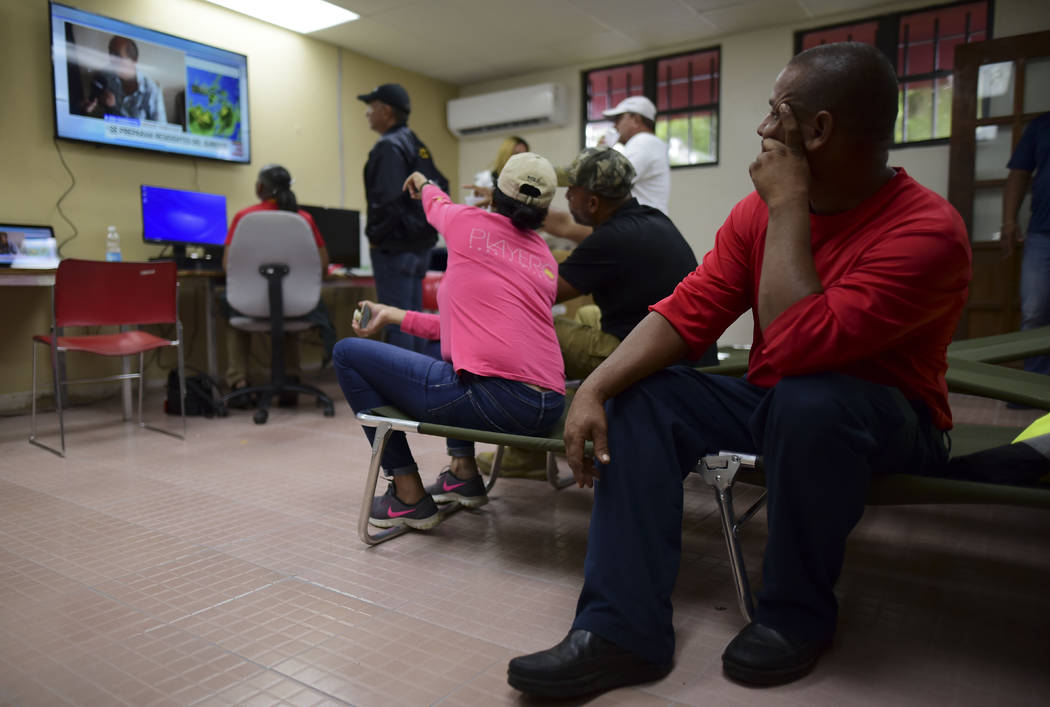 Mayor Rafael Surillo, wearing a blue cap, watches a televised weather report flanked by employe ...