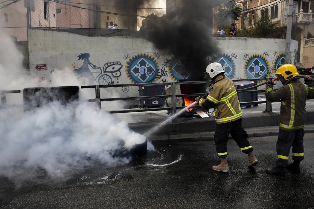 Firefighters extinguish burned tires that were set on fire to block a road during a demonstrati ...