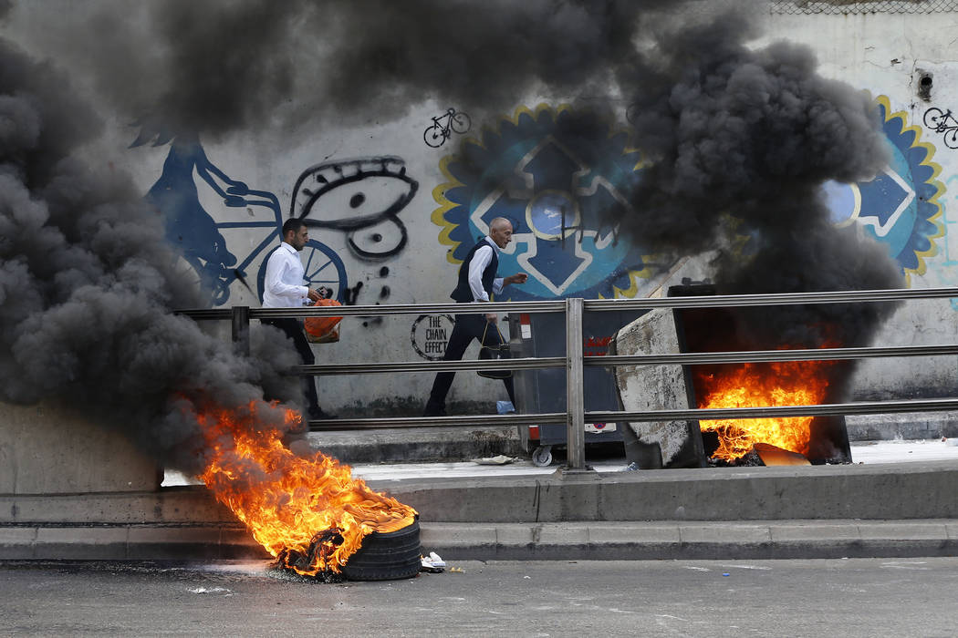 People walk next to tires set on fire by anti-government protesters to block a road during a de ...