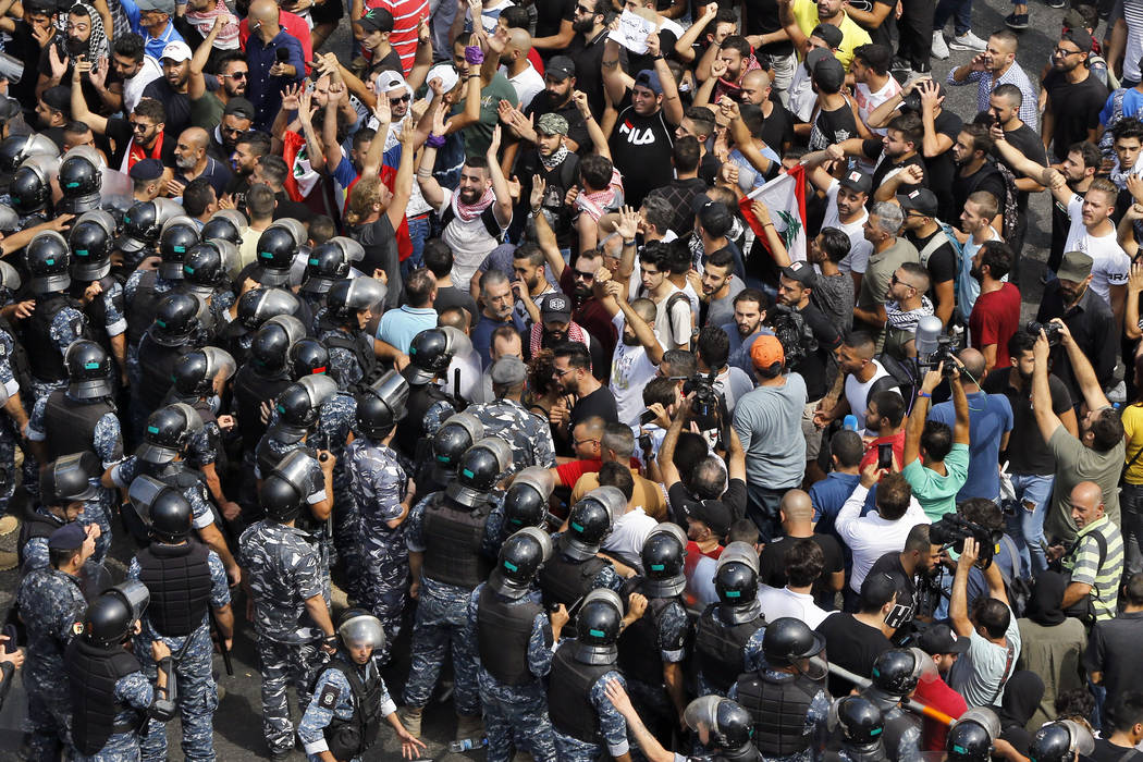 Anti-government protesters chant slogans as riot policemen close the road to the government hou ...