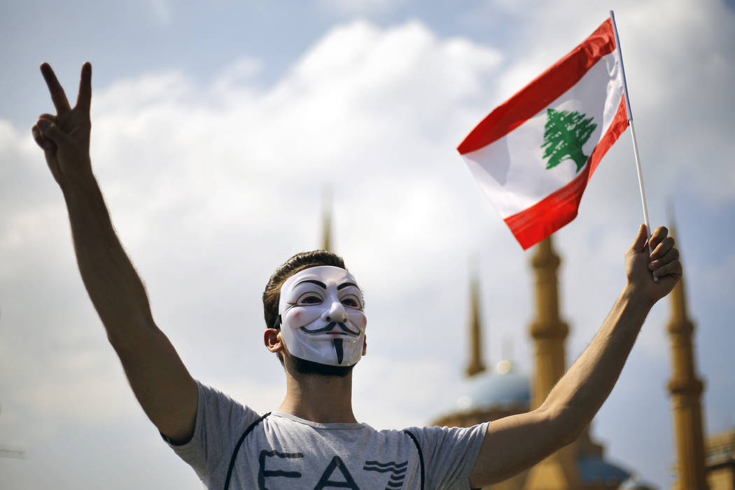 An anti-government protester makes victory sign as he holds a Lebanese flag during a demonstrat ...