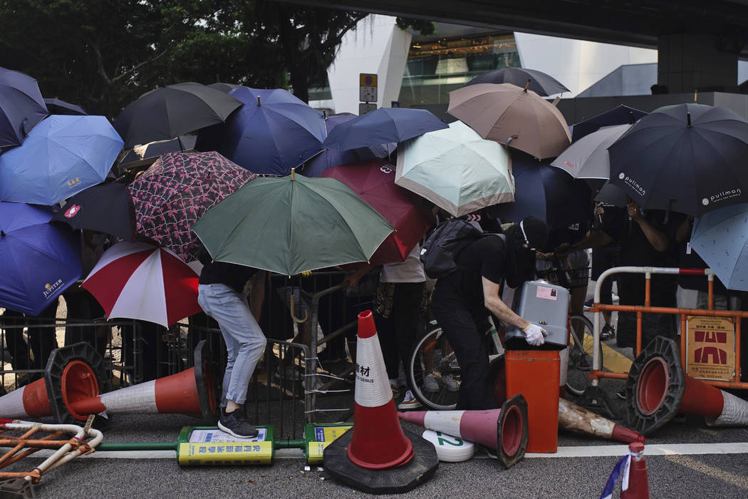 Protesters hide behind umbrellas as they form a barricade to block a road in Hong Kong on Frida ...