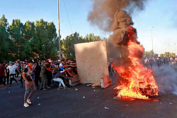 Anti-government protesters set fires and close a street during a demonstration in Baghdad, Iraq ...
