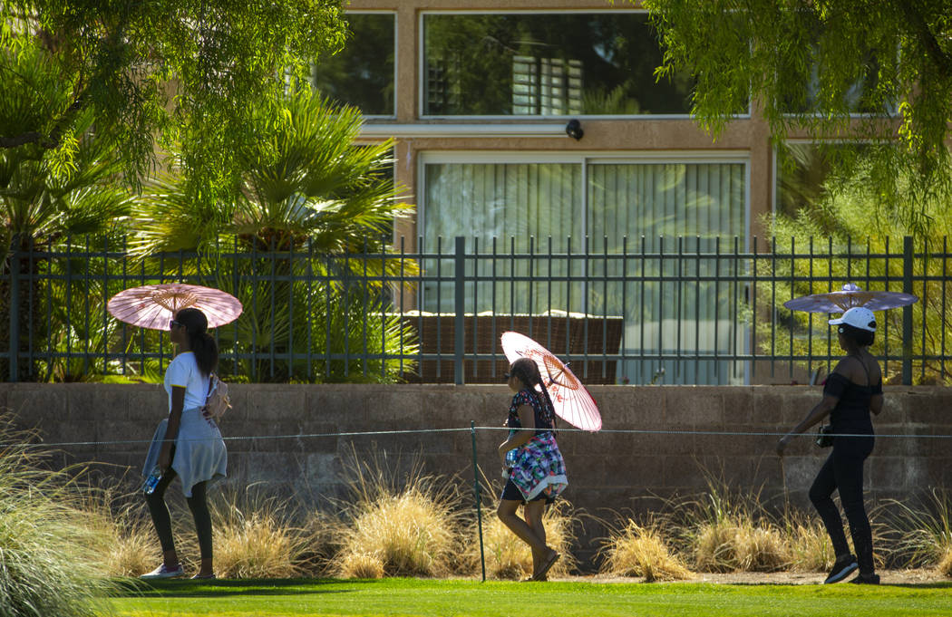 Attendees stay cool under umbrellas as they walk along hole 9 during the final round of Shriner ...