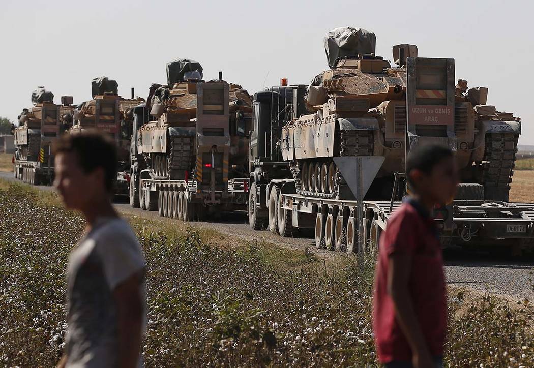 Local residents look on as a convoy of Turkish forces' trucks transporting tanks is driven on a ...