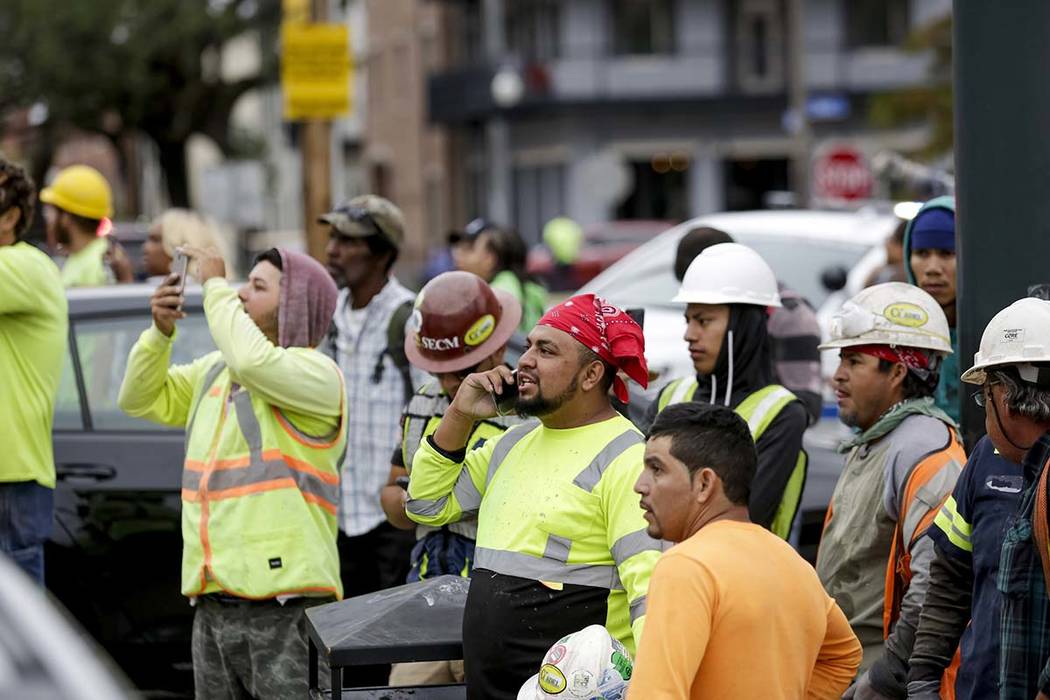 Construction workers look on after a large portion of a hotel under construction suddenly colla ...