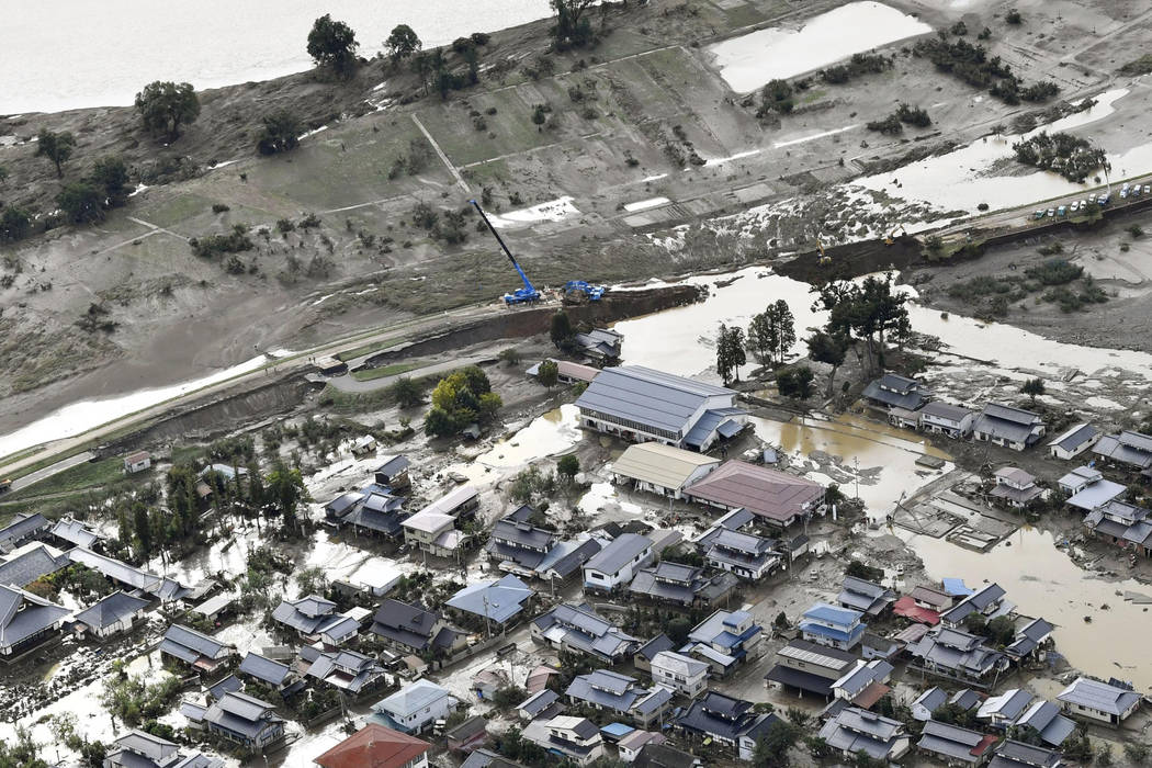 This photo shows a broken embankment, center, of the Chikuma River and flooded residential area ...