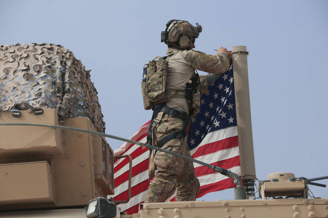 American soldier mount the U.S. flag on a vehicle near the town of Tel Tamr, north Syria, Sunda ...