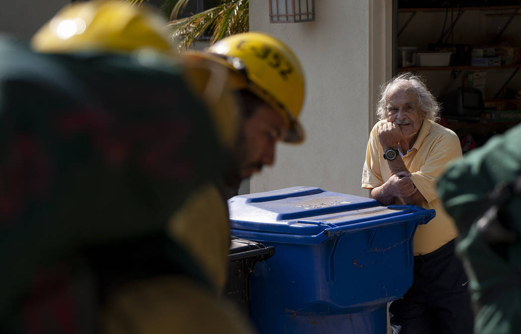 A man watches as firefighters prepare to enter his backyard to fight a wildfire in the Pacific ...