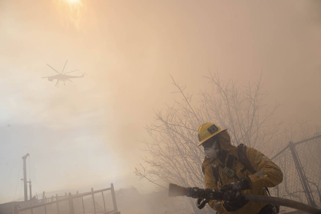 A firefighter carries a hose during work to protect homes from the flames of a wildfire in the ...