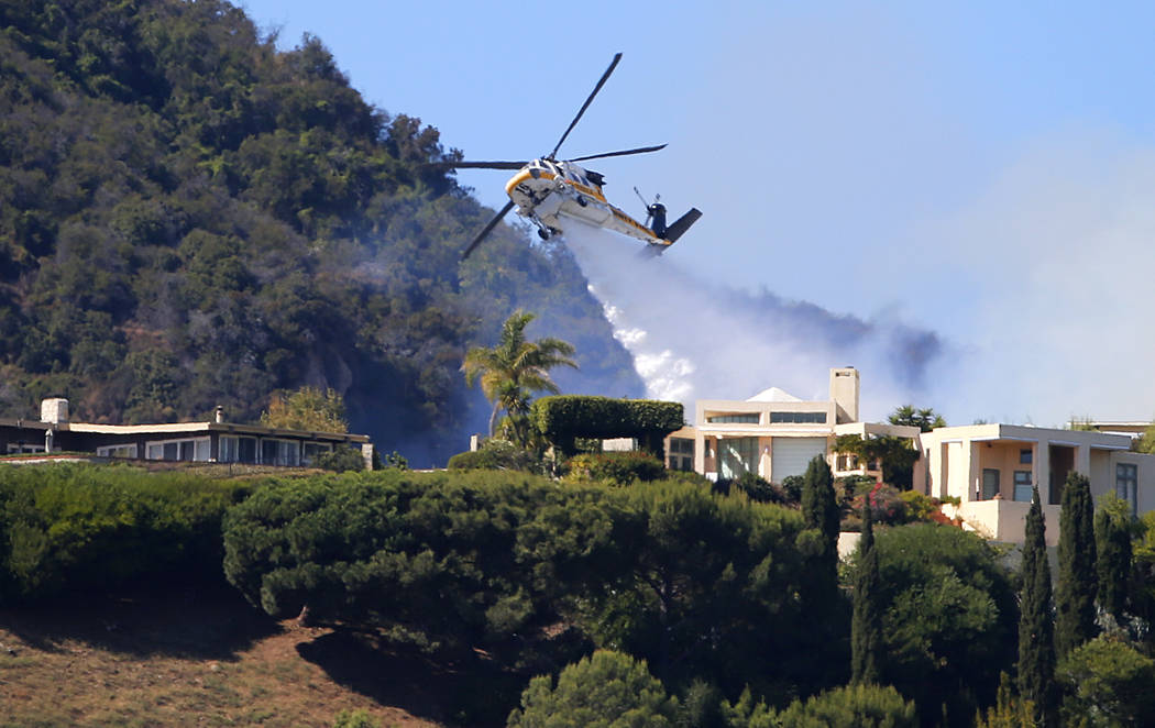 A Los Angeles County Fire Department helicopter makes a water drop as flames from a wildfire th ...