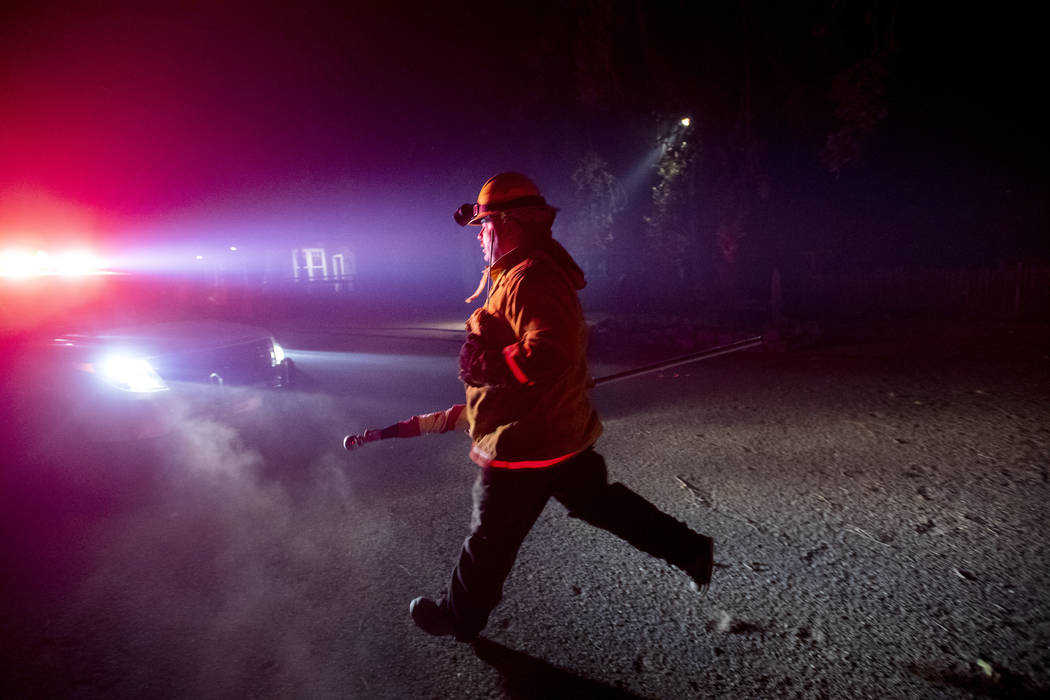 A firefighter from Dry Creek Rancheria carries a flag he removed from a building as the Kincade ...