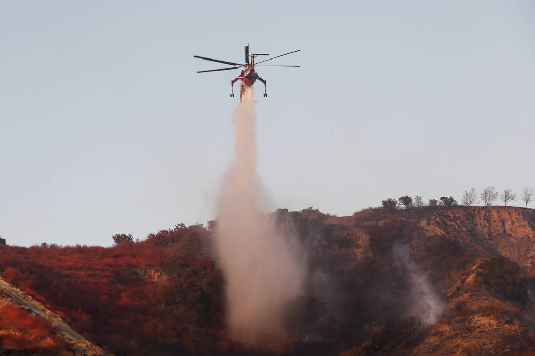A helicopter drops water to put out hotspots in Simi Valley, Calif., Wednesday, Oct. 30, 2019. ...