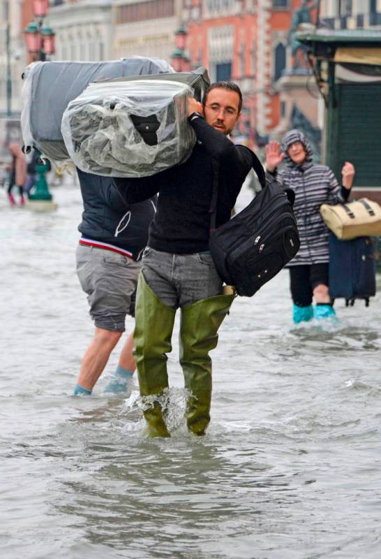 A man carries luggage as he wades in high water, in Venice, Italy, Wednesday, Nov. 13, 2019. Th ...