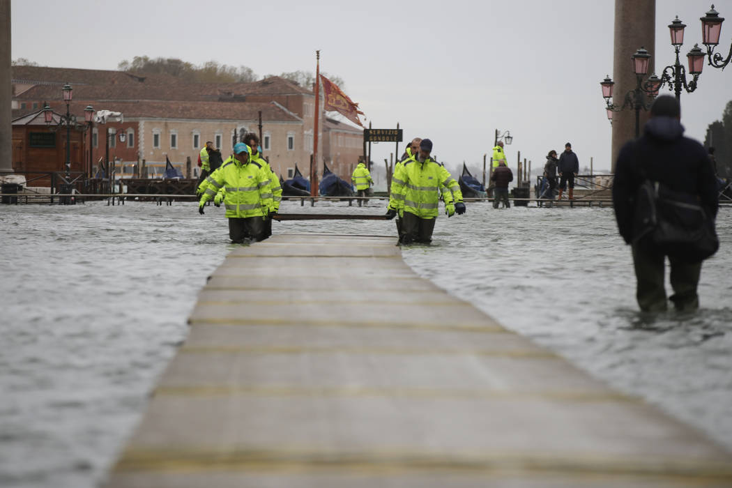 Municipality workers carry wooden boards to make a trestle bridge in a flooded St. Mark's Squar ...