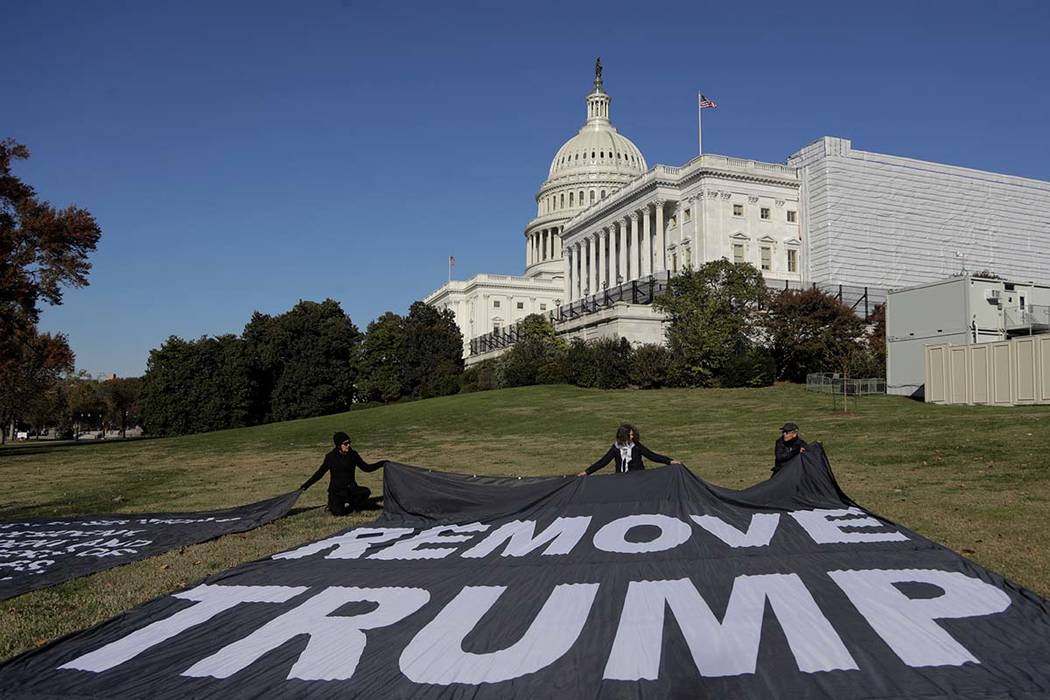 Demonstrators kneel near large banners on the lawn adjacent to the U.S. Capitol, while a top U. ...