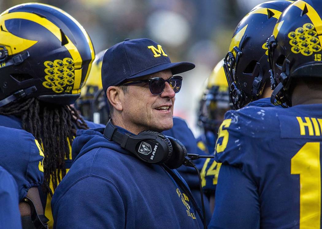 Michigan head coach Jim Harbaugh huddles with his players on the field during a time out in the ...