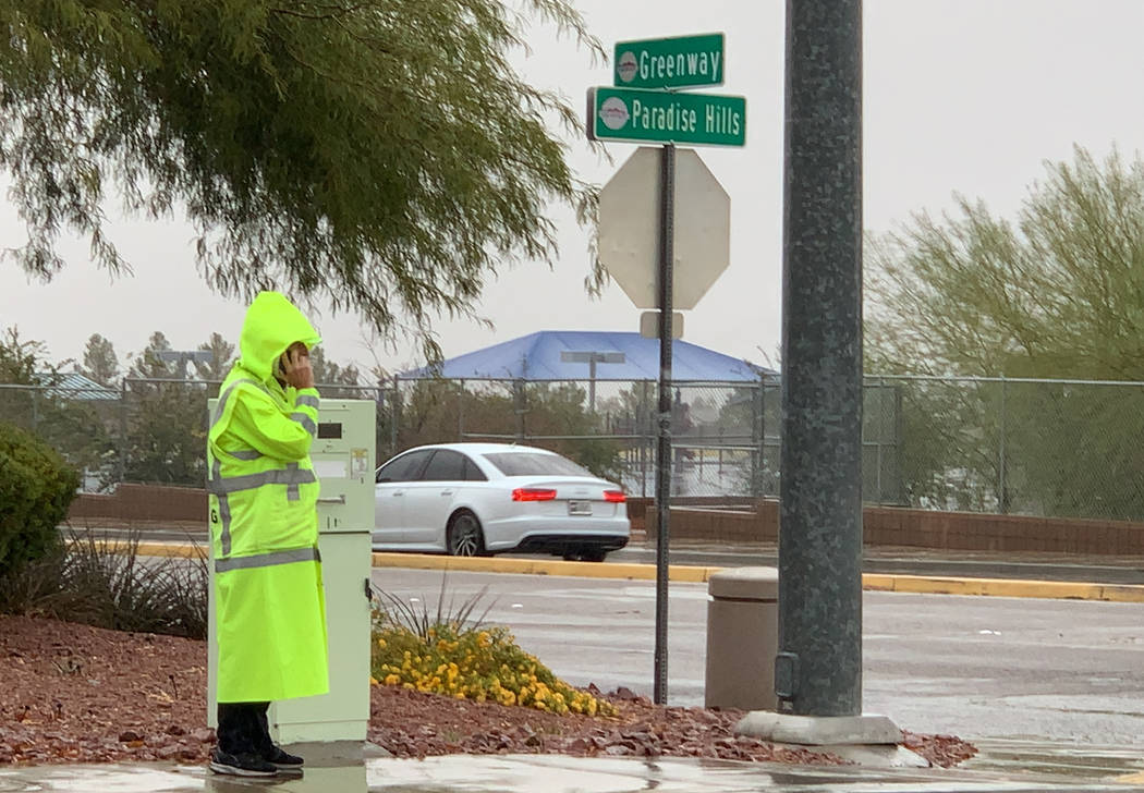 A crossing guard talks on the phone while standing in the rain on a street corner between Smile ...