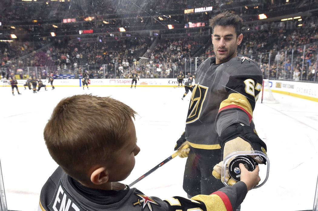 Vegas Golden Knights left wing Max Pacioretty hands a puck though a photographer's hole to a yo ...