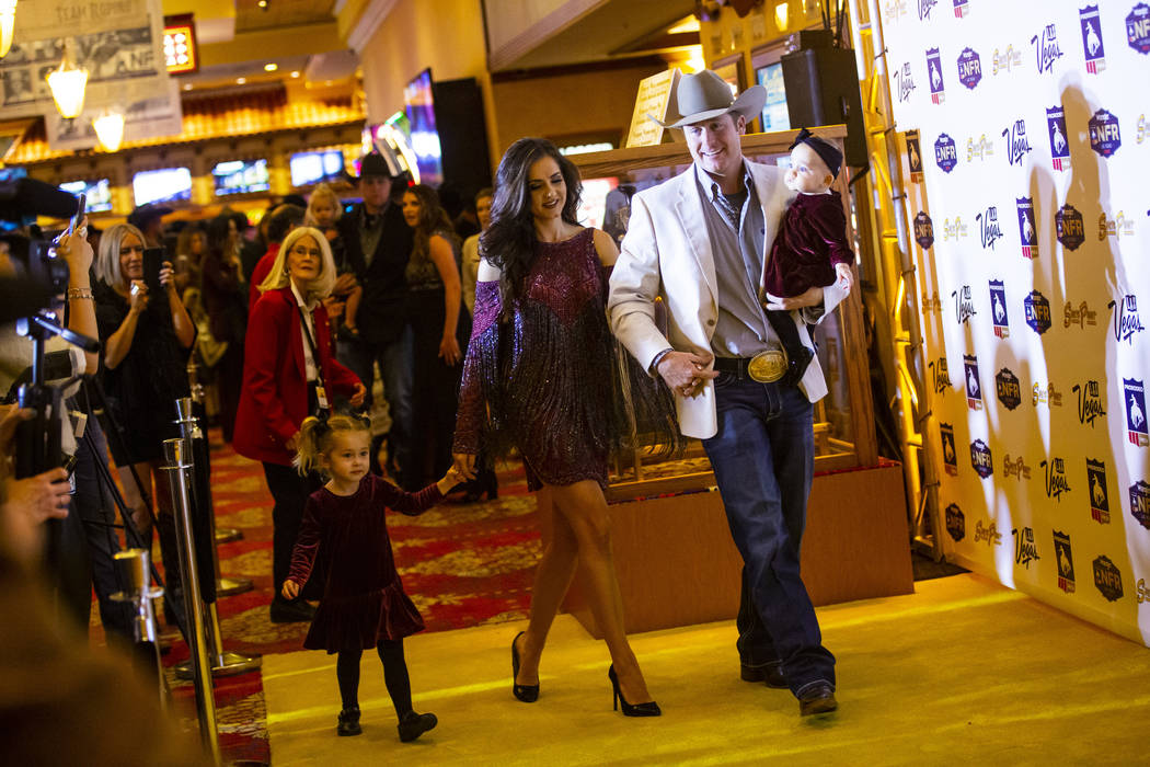 National Finals Rodeo contestant Tyson Durfey, of Brock, Texas, right, walks while holding daug ...