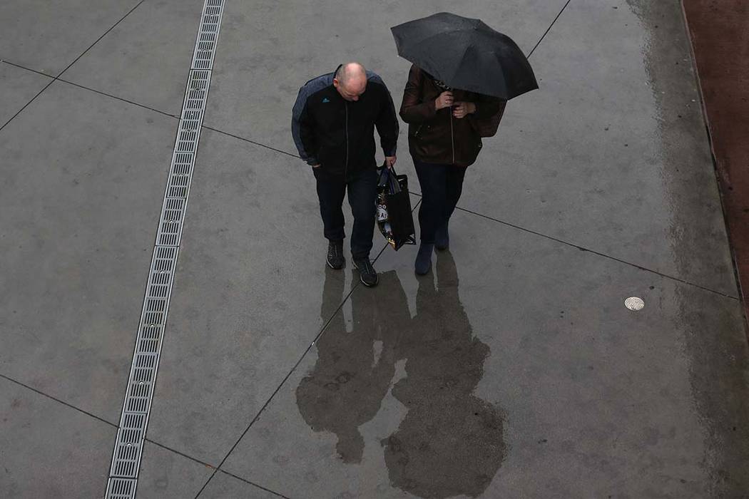 People walk in the rain at the Strip near Bally's casino-hotel in Las Vegas, on Wednesday, Dec. ...