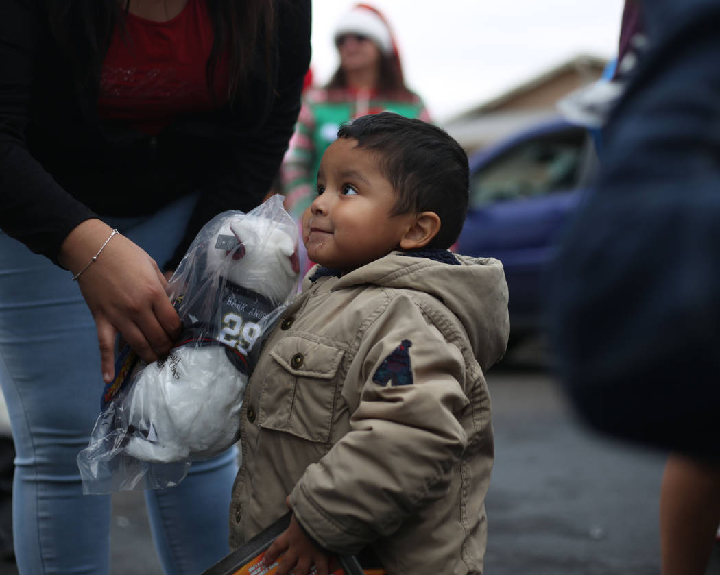 Adan Lopez, 2, looks up at Santa Clause and holds his new stuffed animal provided by the City o ...