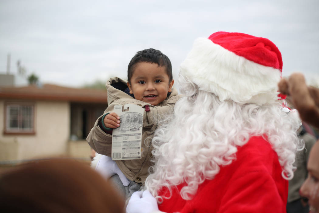 Adan Lopez, 2, is held by Santa after receiving Christmas gifts provided by the City of North L ...