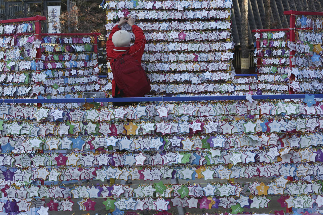 A woman hangs a paper note bearing her New Year wishes to a wire at Jogyesa Buddhist temple in ...