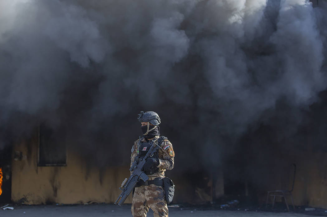 An Iraqi soldier stands guard in front of smoke rising from a fire set by pro-Iranian militiame ...