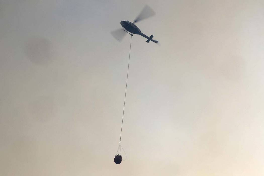 A helicopter carries a water bucket to douse a fire near Bendalong, Australia, Friday, Jan. 3, ...