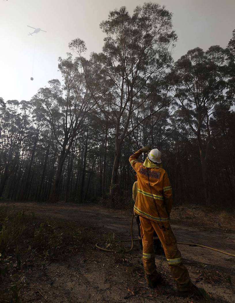 A firefighter watches a water bombing helicopter approach as they battle a fire near Bendalong, ...