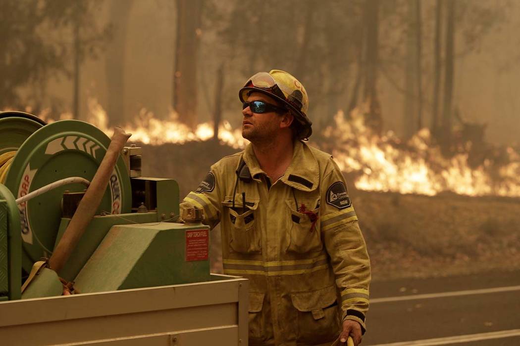 A Forest Corporation worker manages a fire hose as he battles a fire near Moruya, Australia, Sa ...