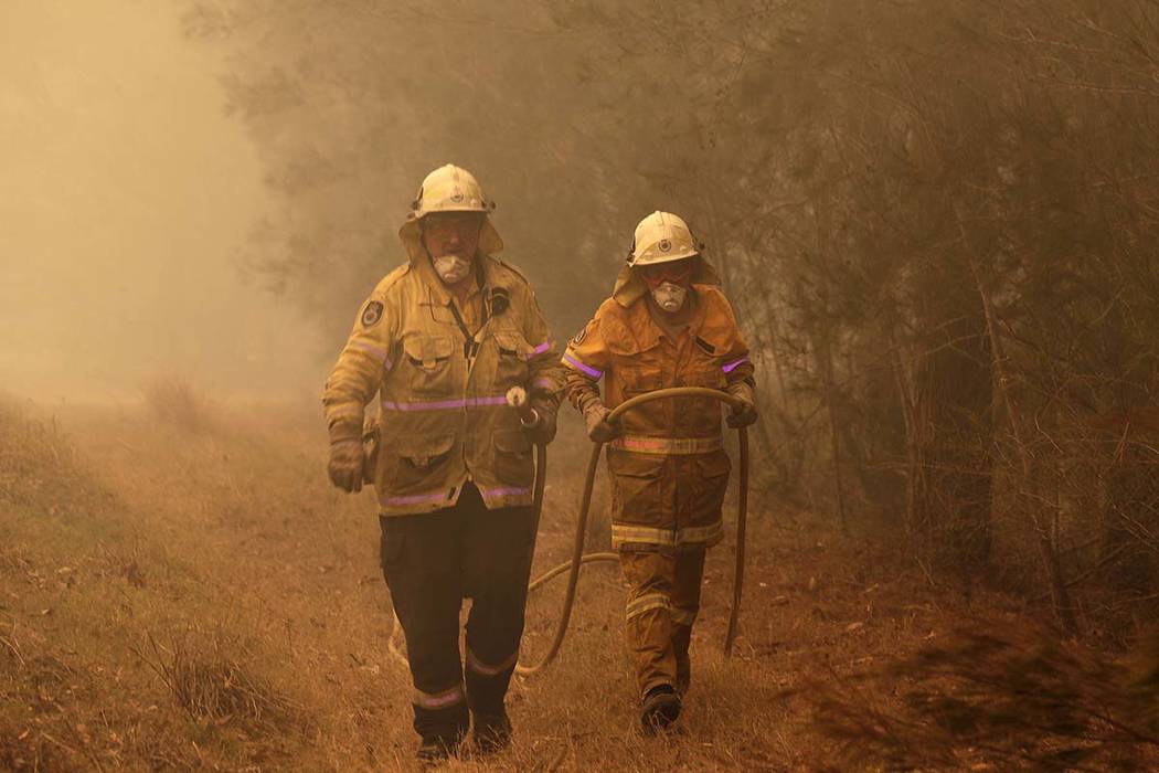 Firefighters drag their water hose after putting out a spot fire near Moruya, Australia, Saturd ...