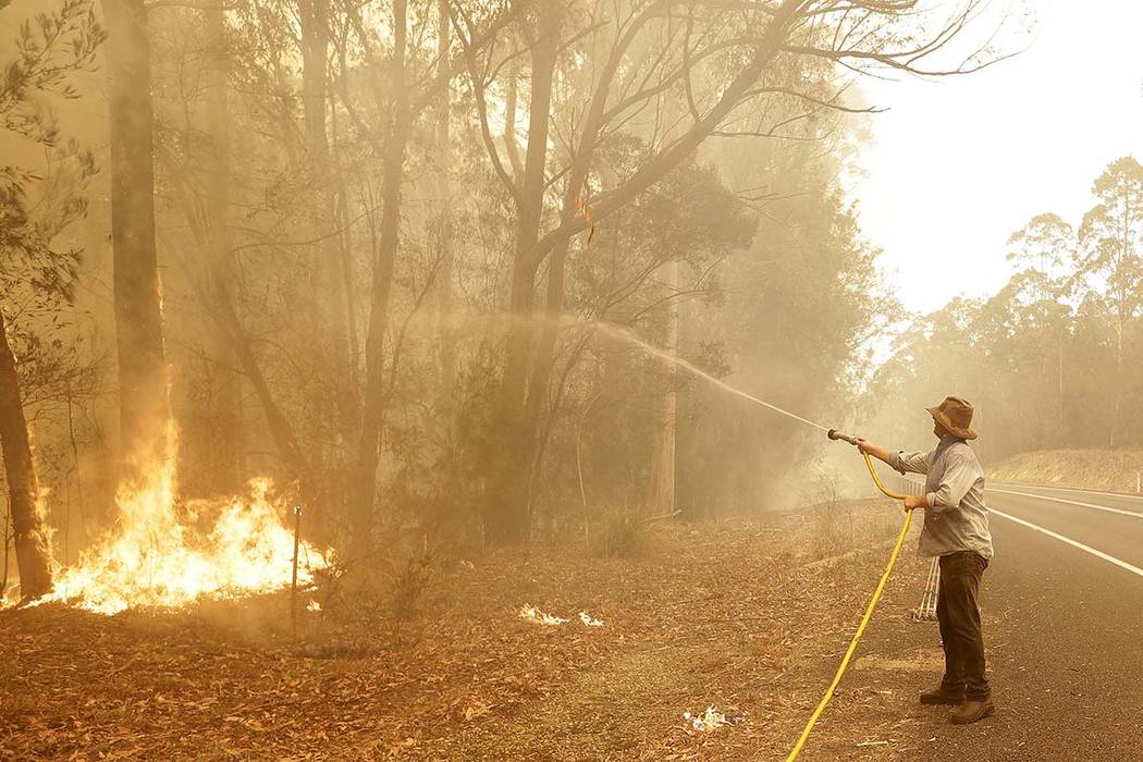 A man uses a water hose to battle a fire near Moruya, Australia, Saturday, Jan. 4, 2020. Austra ...