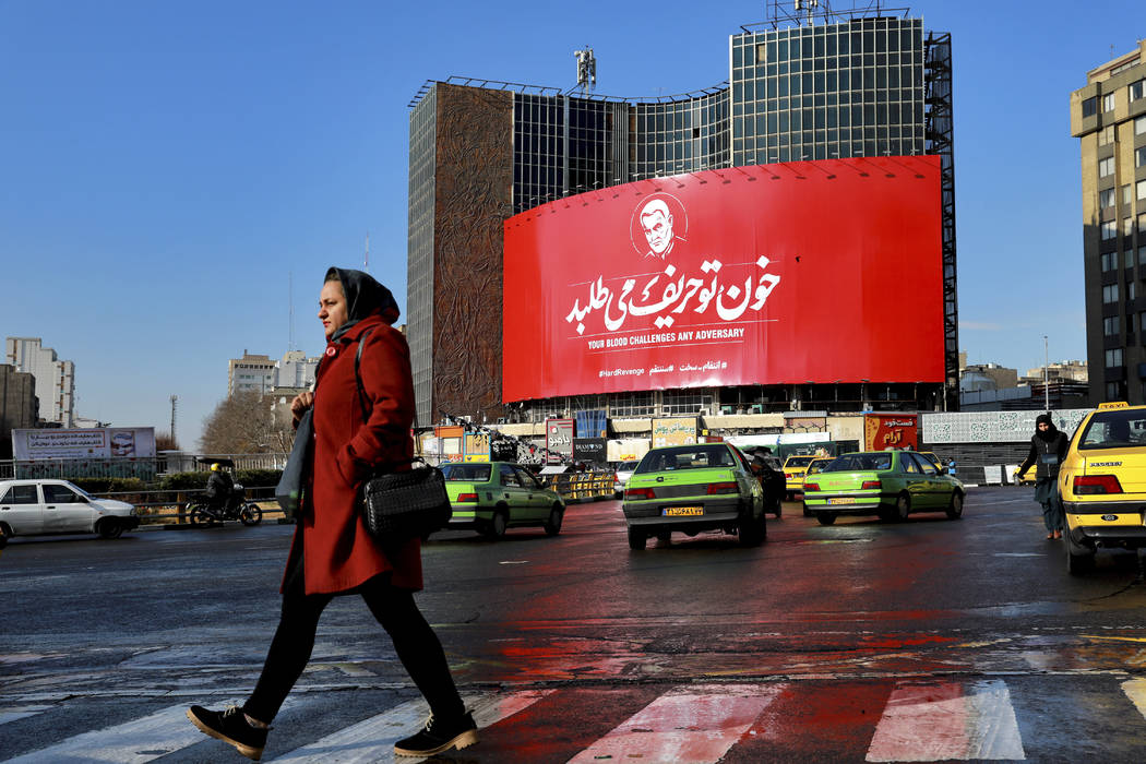 A woman crosses a street in front of a billboard showing a portrait of Iranian Revolutionary Gu ...