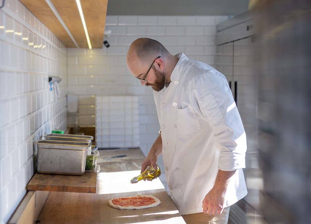 Chef Bartosz Wawrzyszak, owner of the Custom Pizza Truck, drizzles olive oil onto dough while m ...