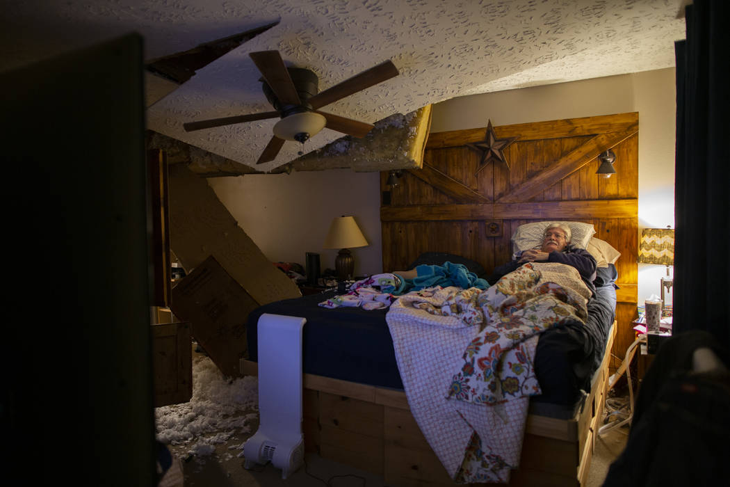 Lee Brewer watches the news from his bedroom as the ceiling hangs after it was damaged by a mas ...