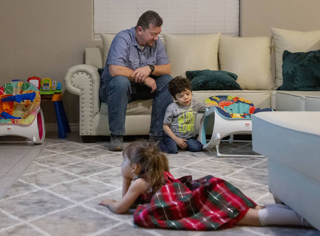 Mike Hansen sits with his children, Luna 2, as she watches a movie, and Rio, 3, plays, at their ...