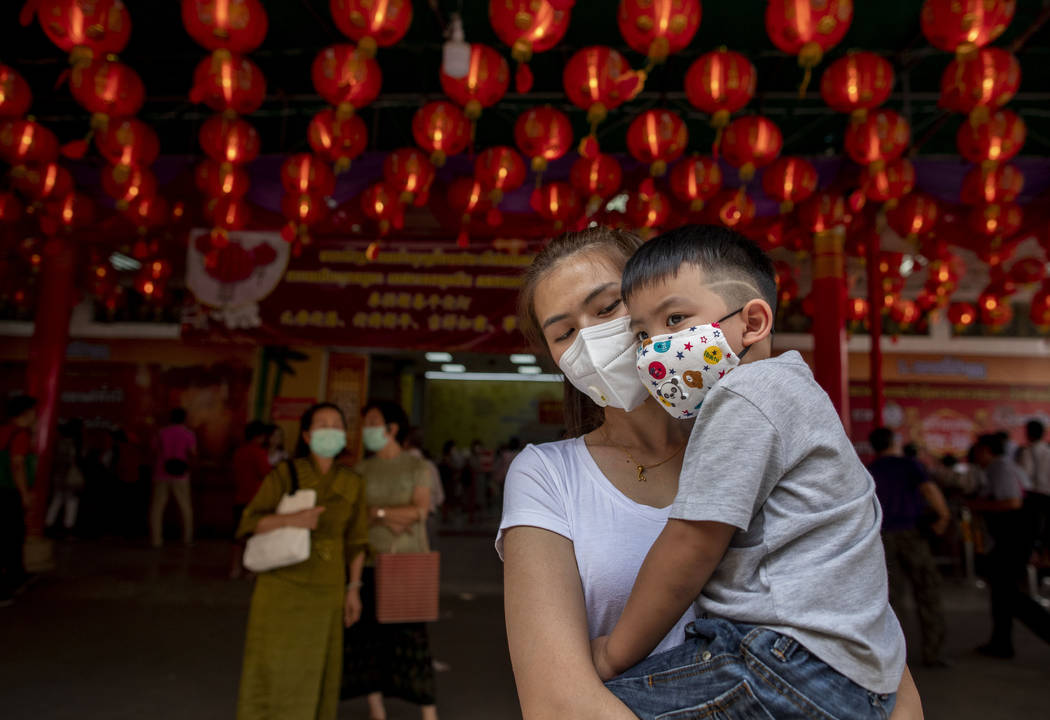 A woman and her child wearing face masks stand in a Chinese temple in Bangkok, Thailand, Thursd ...