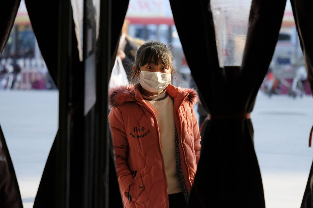 A girl wearing a face mask stands in the entrance to a shop in Wuhan in central China's Hubei P ...