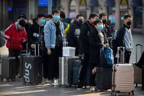 Travelers wear face masks as they stand outside the Beijing Railway Station in Beijing, Friday, ...