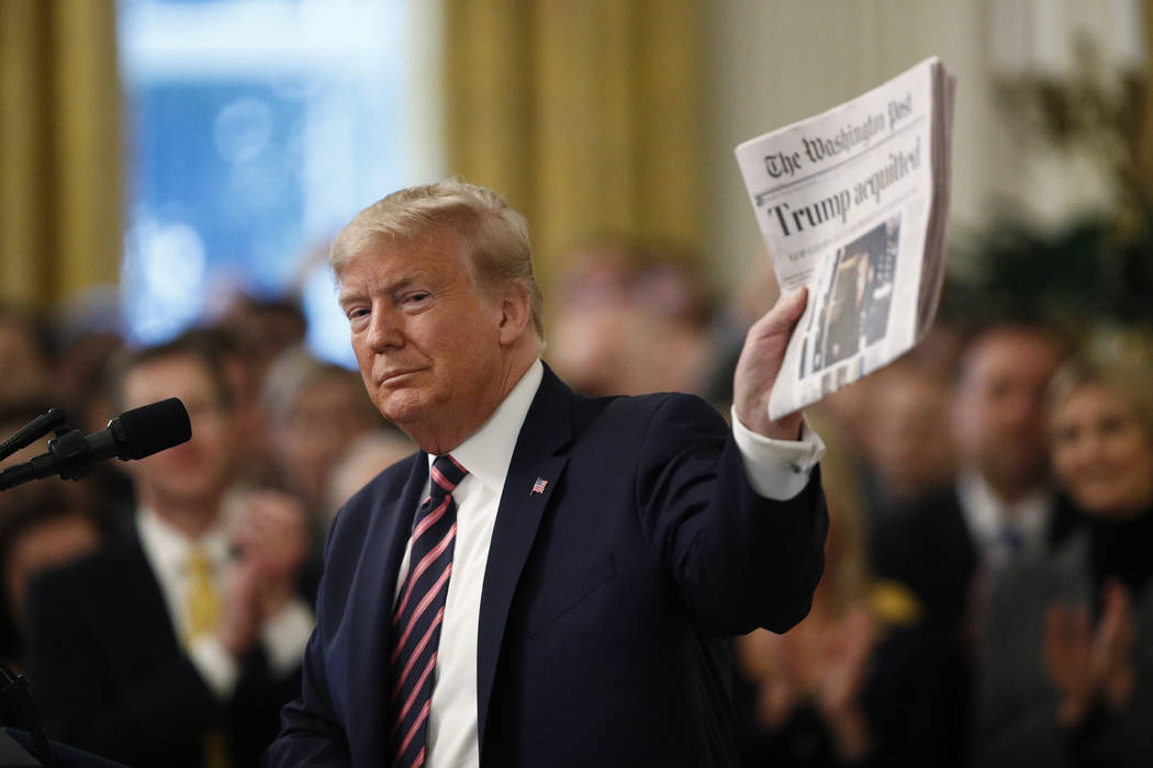 President Donald Trump holds up a newspaper with the headline that reads "Trump acquitted& ...