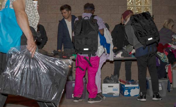 Two individuals wear CITYPAK backpacks as they look through donated clothing as a person walks ...