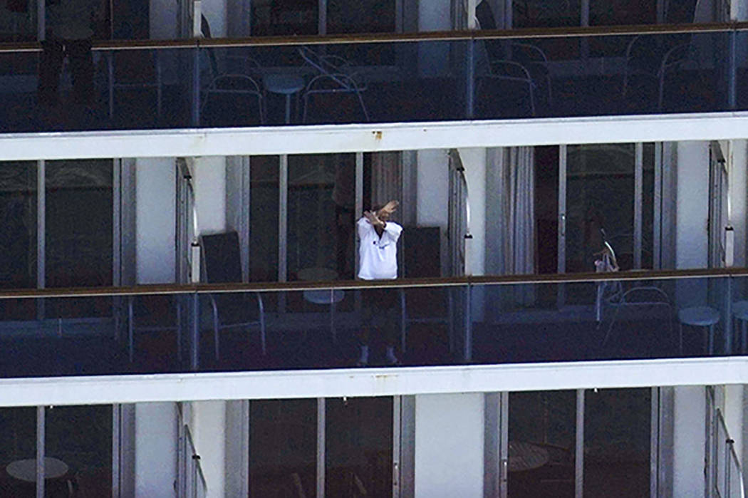 A passenger waves from the cruise ship Diamond Princess anchored off Yokosuka, near Tokyo, Satu ...