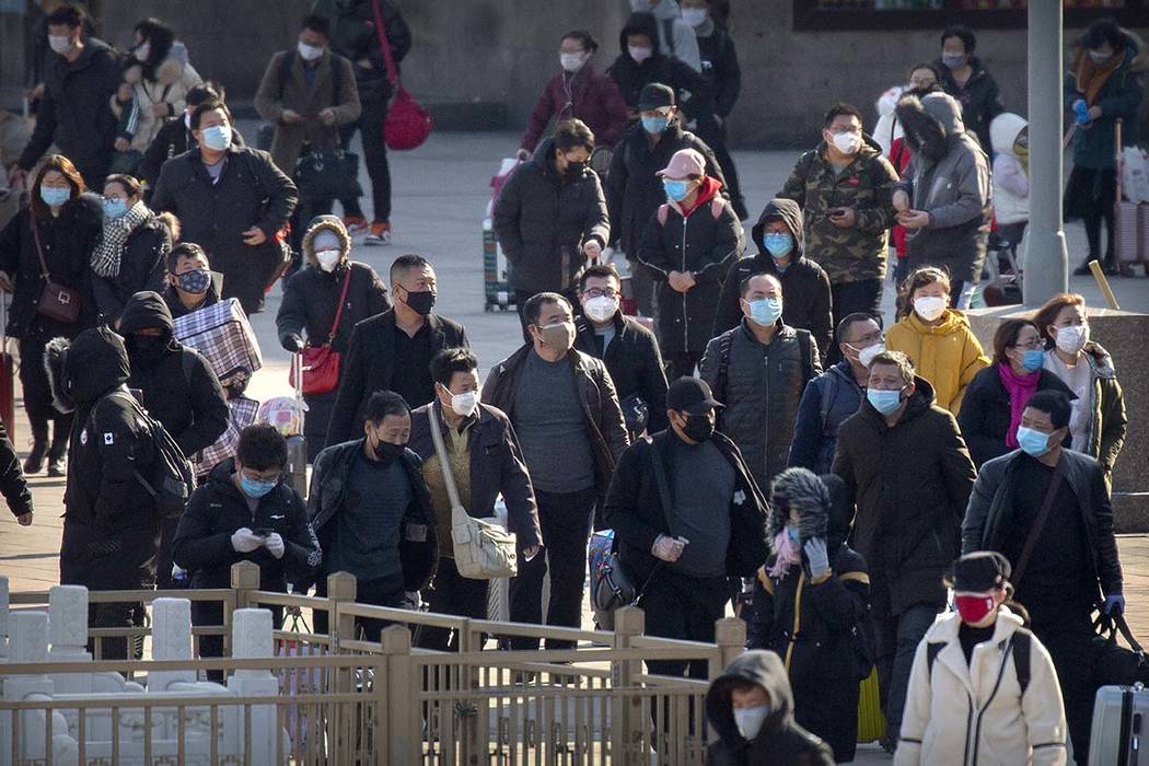 Travelers wear face masks as they walk outside the Beijing Railway Station in Beijing, Saturday ...
