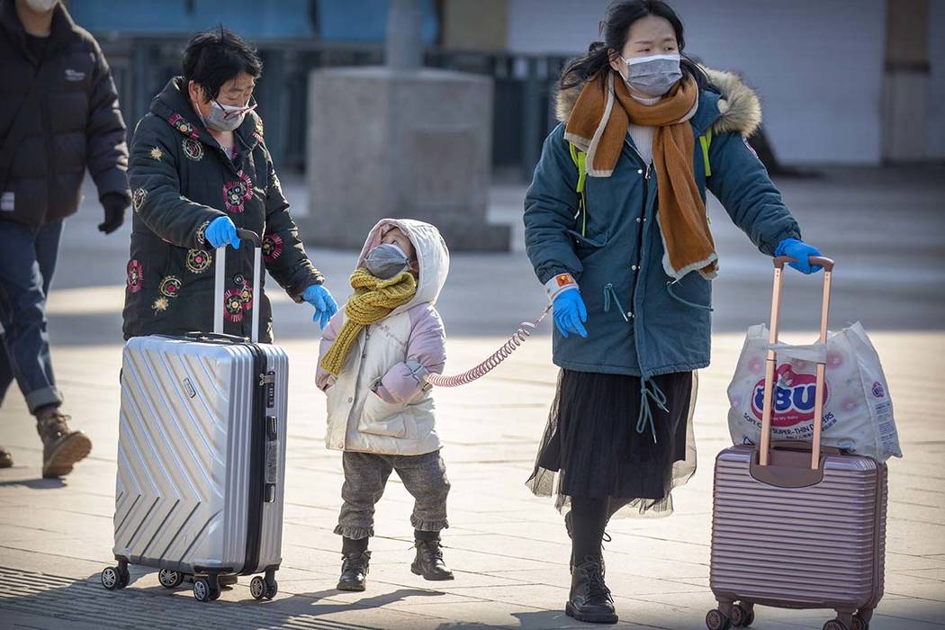 Travelers wear face masks as they walk outside the Beijing Railway Station in Beijing, Saturday ...